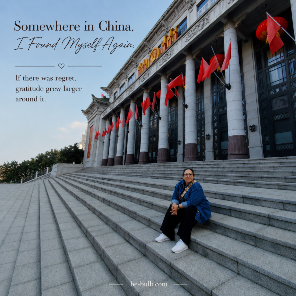 Real photograph of Lia sitting on broad stone steps outside a grand building in Haikou, overlaid with the words Somewhere in China, I Found Myself Again.